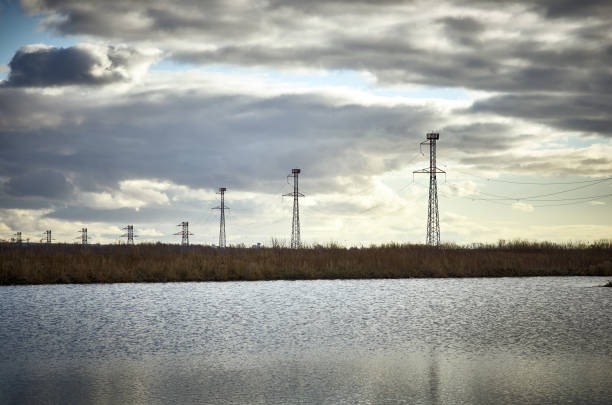 istock High voltage power tower pylon, lake water cloudy sky 1177097118
