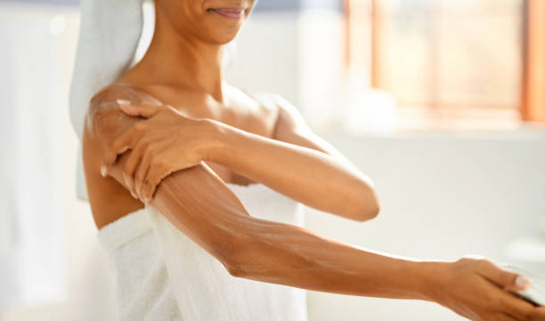 Keep your skin fresh and smooth Close-up of a woman wrapped in towel after bath applying moisturizer on her arm rubbing arm stock pictures, royalty-free photos & images