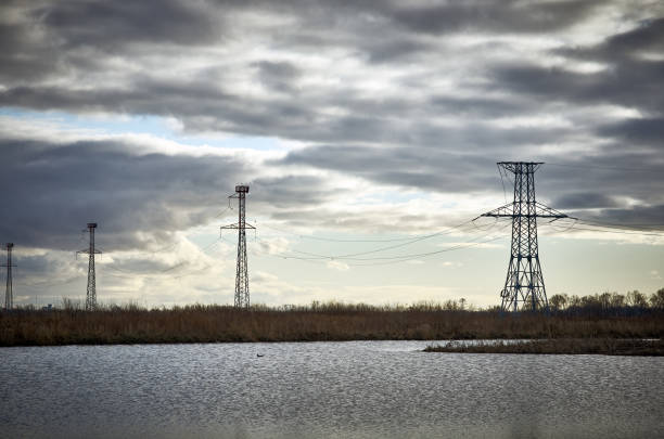 istock High voltage power tower pylon, lake water cloudy sky 1177098561