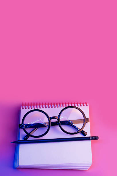 istock black round glasses lie on a Notepad in neon light on pink background 1177101571