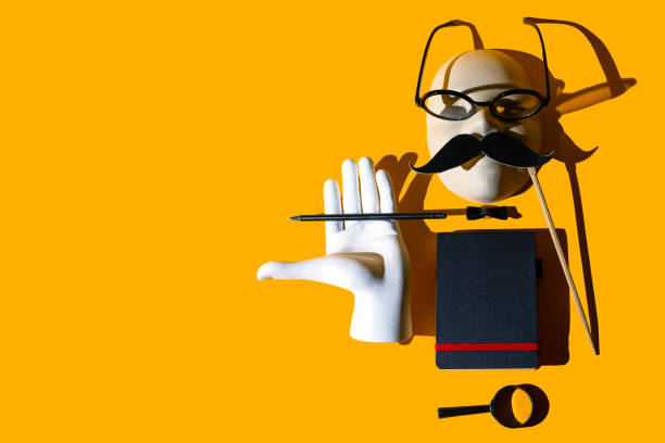 istock composition of various objects. Glasses, magnifying glass, pencil, mustache, butterfly, hand, notebook, mask. Form the image of a business person. Hard shadows on a yellow background 1177103980
