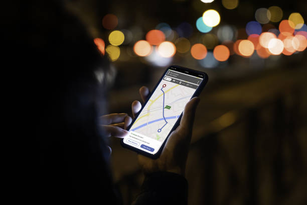 Woman looking at lit phone with navigation map photographed at night in a city stock photo