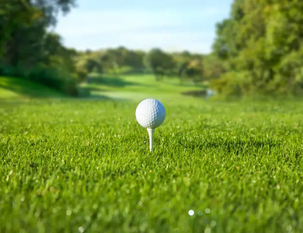 Low angle, selective focus view of golf ball on a tee in front of a sunny fairway