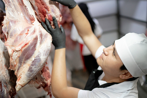 Butcher cutting a piece of meat inside the meat locker