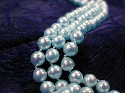 Multicolored Pearl necklaces on pink silk fabric background.
