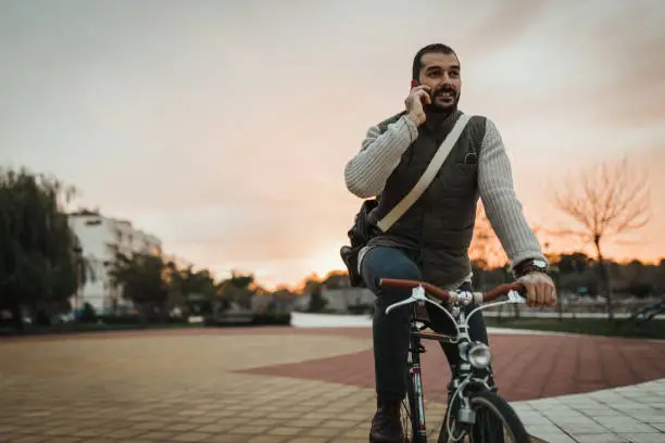 Photo of Man driving a bicycle in the city park and using a smart phone