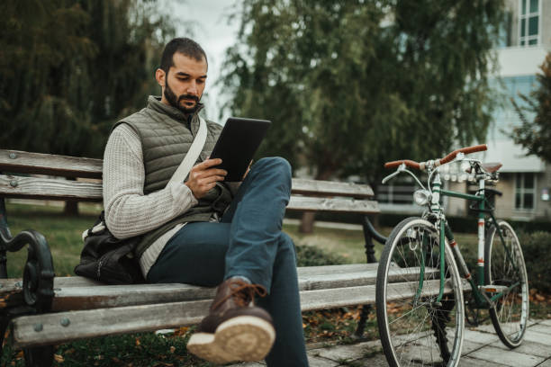 istock Man with a bicycle sitting on the park bench and using digital tablet 1177111696