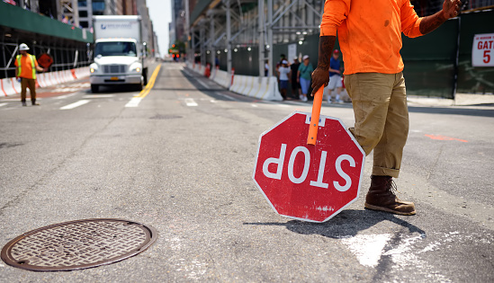 New York, USA - July 9, 2019: Black road worker carries a Stop sign down a new York city street. He stops the movement during construction. Construction new skyscraper in NYC.