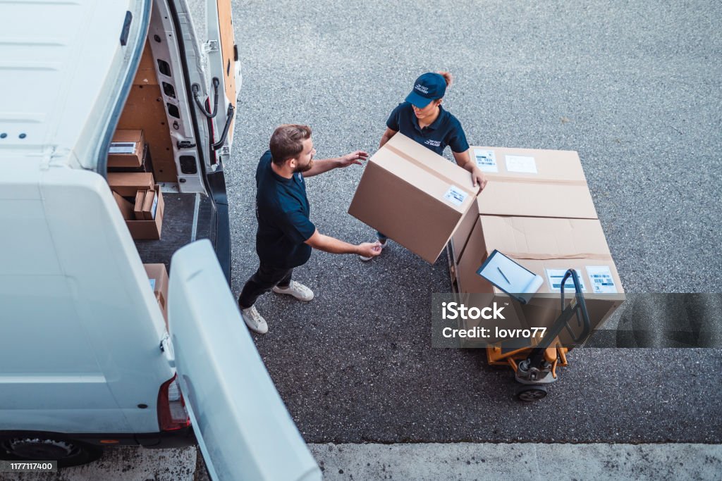 Coworkers rushing to load packages in a delivery van Delivery workers using a Hydraulic Hand Pallet Truck to load a delivery van. Delivering Stock Photo