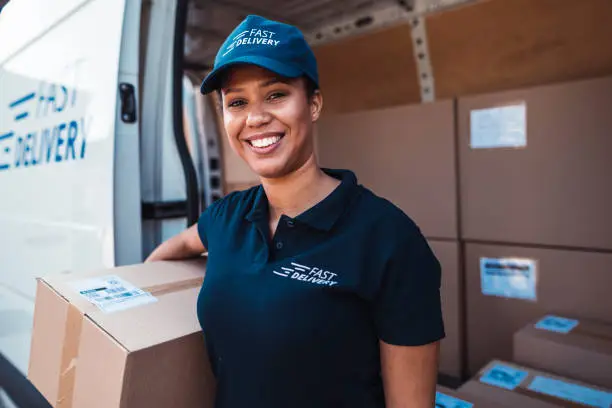 African-American woman holding a delivery package in front of delivery van.