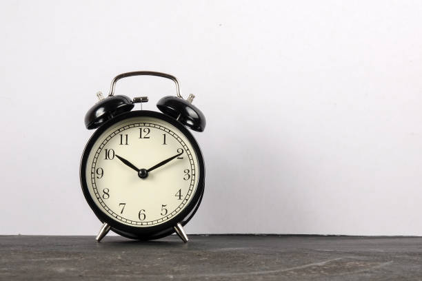 istock Black alarm clock on the wooden surface against the white background. 1177125308