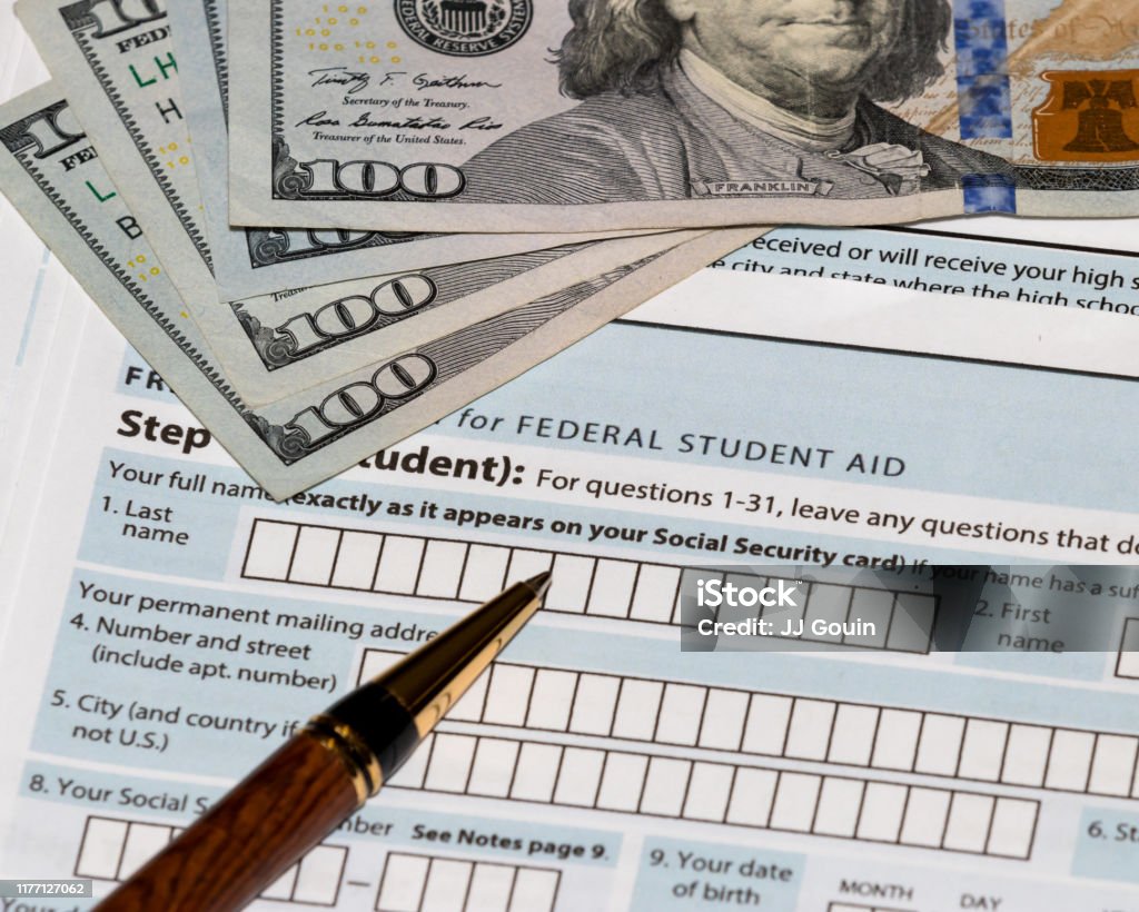 Student financial aid application forms for college tuition loans and grants with one-hundred dollar bills and ballpoint pen landscape, no people, student loan debt crisis Student Financial Aid Stock Photo