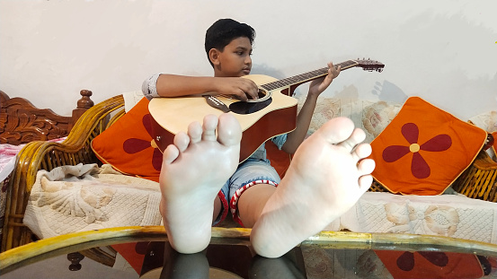 Time to take a break from his studies.  This Young Indian Boy is Practicing his Guitar, while relaxing in his Bedroom.