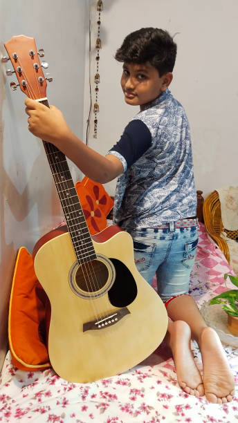 A Barefoot Young Boy in India Practices his Guitar in his Bedroom