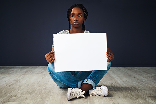 Studio shot of a beautiful young woman holding a blank placard against a black background