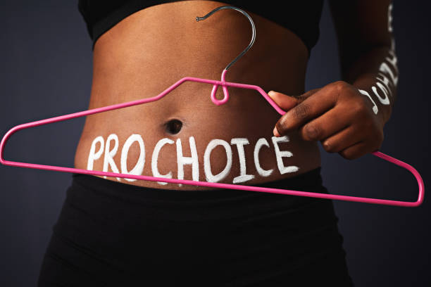 I choose what's right for me Cropped studio shot of a woman holding a hanger with “pro choice” painted on her stomach against a dark background reproductive rights stock pictures, royalty-free photos & images