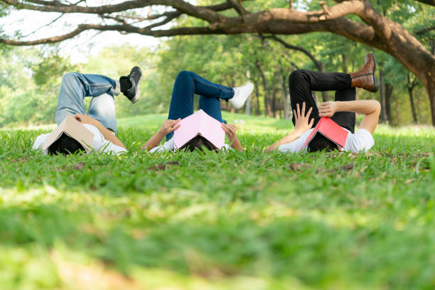 Girls lying on the grass using a tablet. Girls watching video on tablet outdoors. Primary school students on summer vacation.