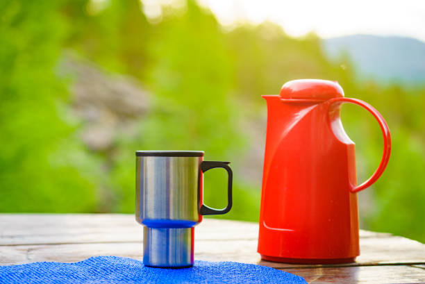 Picnic site table with thermos and thermal mug, norwegian mountains nature in the background. Camping with thermos.