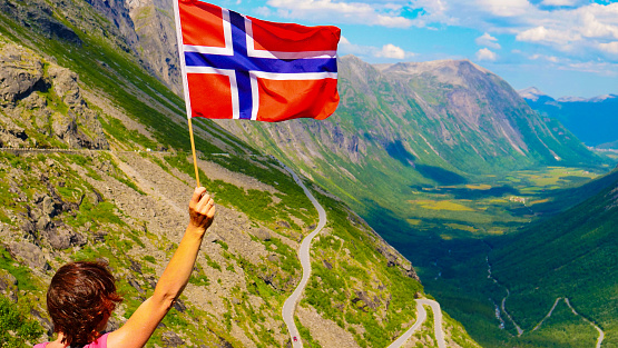 Tourist woman with norwegian flag on Trollstigen viewpoint. Trolls Path mountain road in Norway. National route. Touristic attraction.