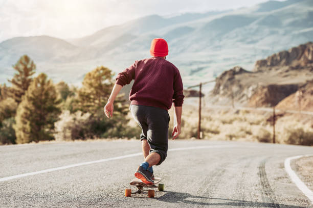 Man hipster is skateboarding at mountain road in sunset light