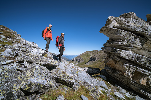 sporty mature adult couple hiker mountaineers with backpacks  hiking together  in rocky cliffy mountains high above timber line on sunny day with clear blue sky