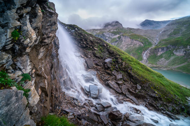 long exposure shot of beautiful waterfall over rocks and stones high up in european mountains alps with lake on cold summer day nobody