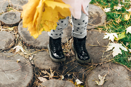 Black boots of little fashionable toddler girl in autumn park.Nature background.