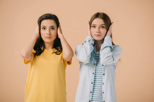 istock attractive friends touching their ears and looking at camera isolated on beige 1177185066