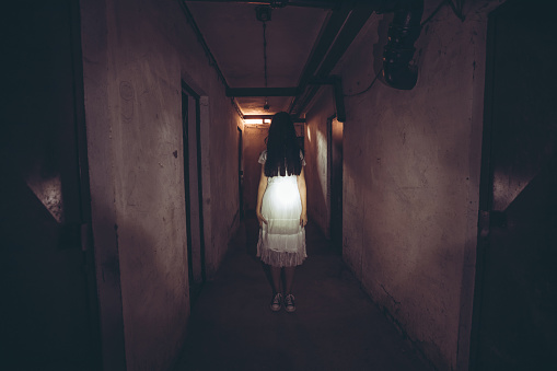 Scary ghost of a woman standing in dark basement corridor.