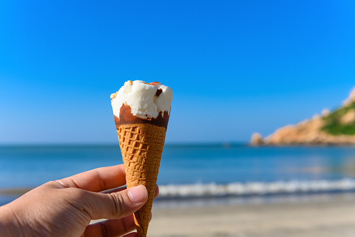 hand holding an ice cream cone in front of an ocean with soft wave