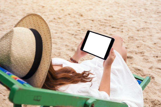 istock a woman holding a black tablet pc with blank desktop screen while lying down on a beach chair 1177188044