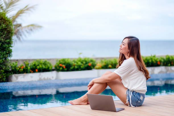 istock woman sitting by swimming pool with laptop computer 1177188198