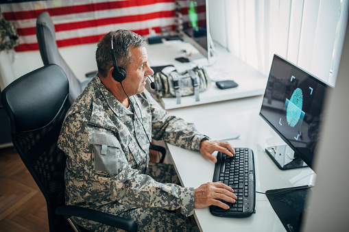 One mature man, American soldier sitting in headquarters office alone, using computer.