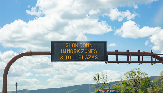 Pennsylvania highway, USA. May 6, 2019: Slow down in work zones and toll plazas Warning led road sign billboard on a highway, cloudy blue sky
