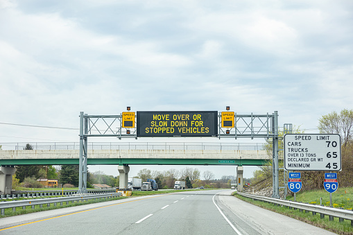 Illinois highway, USA. May 8, 2019: Warning road sign billboard for stopped vehicles and speed limits on a highway, cloudy sky