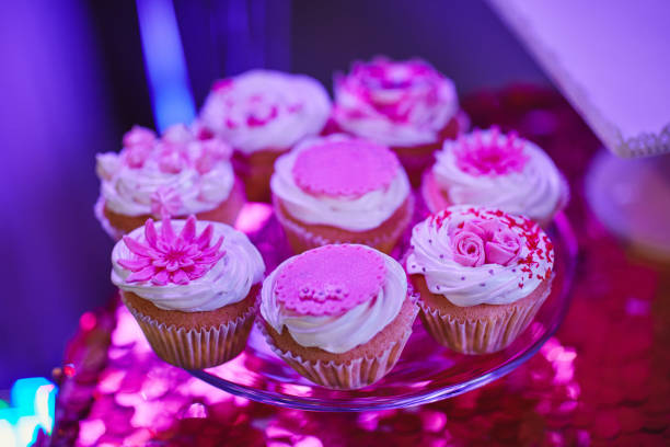 Set of different delicious tasty muffins on table festive background with shiny pink tablecloth. Different dessert tartlets with decorated cream and pink scenery . Selective focus. Candy bar concept