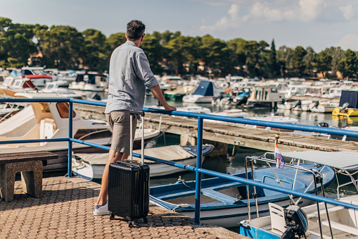 One man, modern gentleman tourist with suitcase standing by the sea.