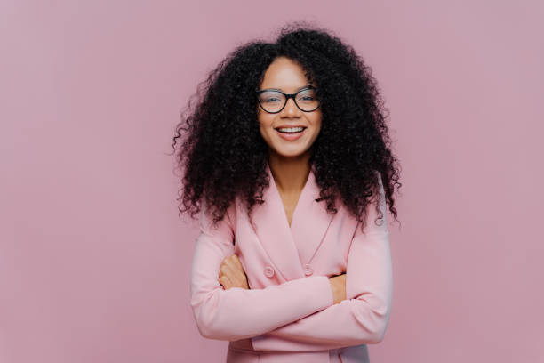 istock Pleased curly haired woman wears optical glasses for vision correction, elegant suit, keeps hands crossed over chest, poses against purple background, comes on job interview. Businesswoman at work 1177211783