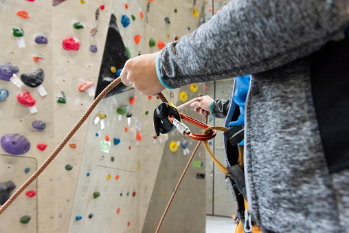 Rock wall climber wearing safety harness and climbing equipment indoor, close-up