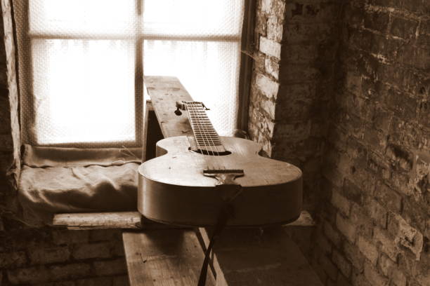 An old wooden guitar with all strings attached to it laying on a wooden bench or table inside an abandoned shack or hut made out of white brick, next to an old glass window seen on a sunny summer day una vieja guitarra de madera con todas las cuerdas unidas a ella tendida en un banco o mesa de madera dentro de una choza o choza abandonada hecha de ladrillo blanco, junto a una vieja ventana de cristal vista en un día soleado de verano