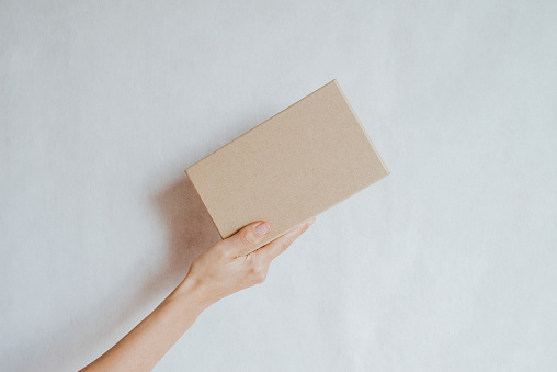 Woman holding in hand small paper box. Young girl with new package. Postal service, delivery. Craft paper. Gift box, present. Box closeup. Blank packing, empty space. People communication. Carton case