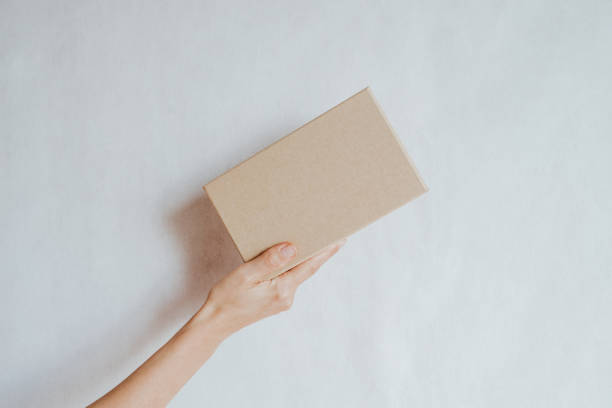 Woman holding in hand small paper box. Young girl with new package. Postal service, delivery. Craft paper. Gift box, present. Box closeup. Blank packing, empty space. People communication. Carton case stock photo