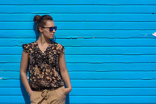 Cute girl in front of a blue wooden wall, a woman with sunglasses on a blue background. Looks into the distance.