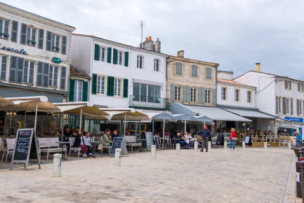 Traditional French street cafes on quayside of La Flotte village on Ile de Re island in France Isle of Re, France - May 09, 2019: People relax in traditional French street cafes on quayside of La Flotte village on Ile de Re island in France flotte stock pictures, royalty-free photos & images