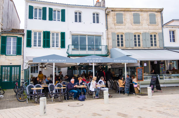 Traditional French street cafes on quayside of La Flotte village on Ile de Re island in France Isle of Re, France - May 09, 2019: People relax in traditional French street cafes on quayside of La Flotte village on Ile de Re island in France flotte stock pictures, royalty-free photos & images