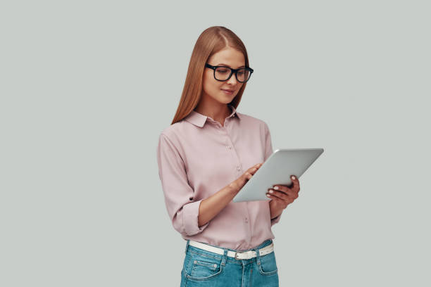 istock Attractive young woman in eyewear using digital tablet and smiling while standing against grey background 1177220497