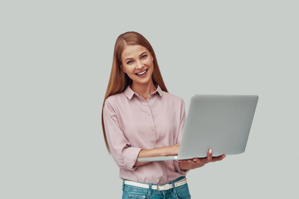 istock Attractive young woman using laptop and smiling while standing against grey background 1177220737
