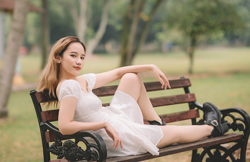 an asian female teenager girl sitting on the wooden bench at public park