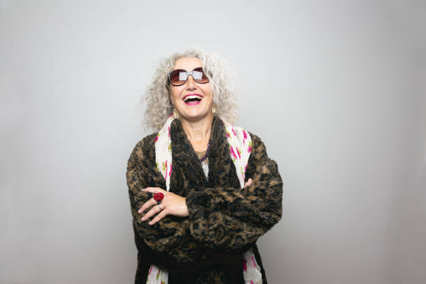 Cool senior woman with sunglasses Cool mature woman,wearing sunglasses and a coat made from artificial fur, wearing scarf with floralpattern and a lot of jewellery, she is standing in front of grey background,looking into camera,smiling hippie photos stock pictures, royalty-free photos & images