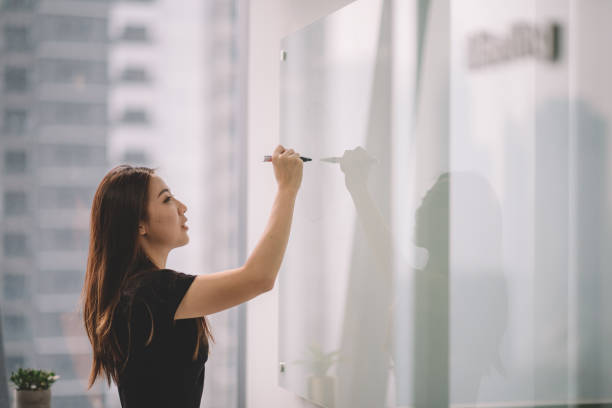 una donna cinese asiatica che scrive su lavagna bianca con la pennarello durante la riunione della conferenza nella sala conferenze dell'ufficio - business plan new business planning foto e immagini stock